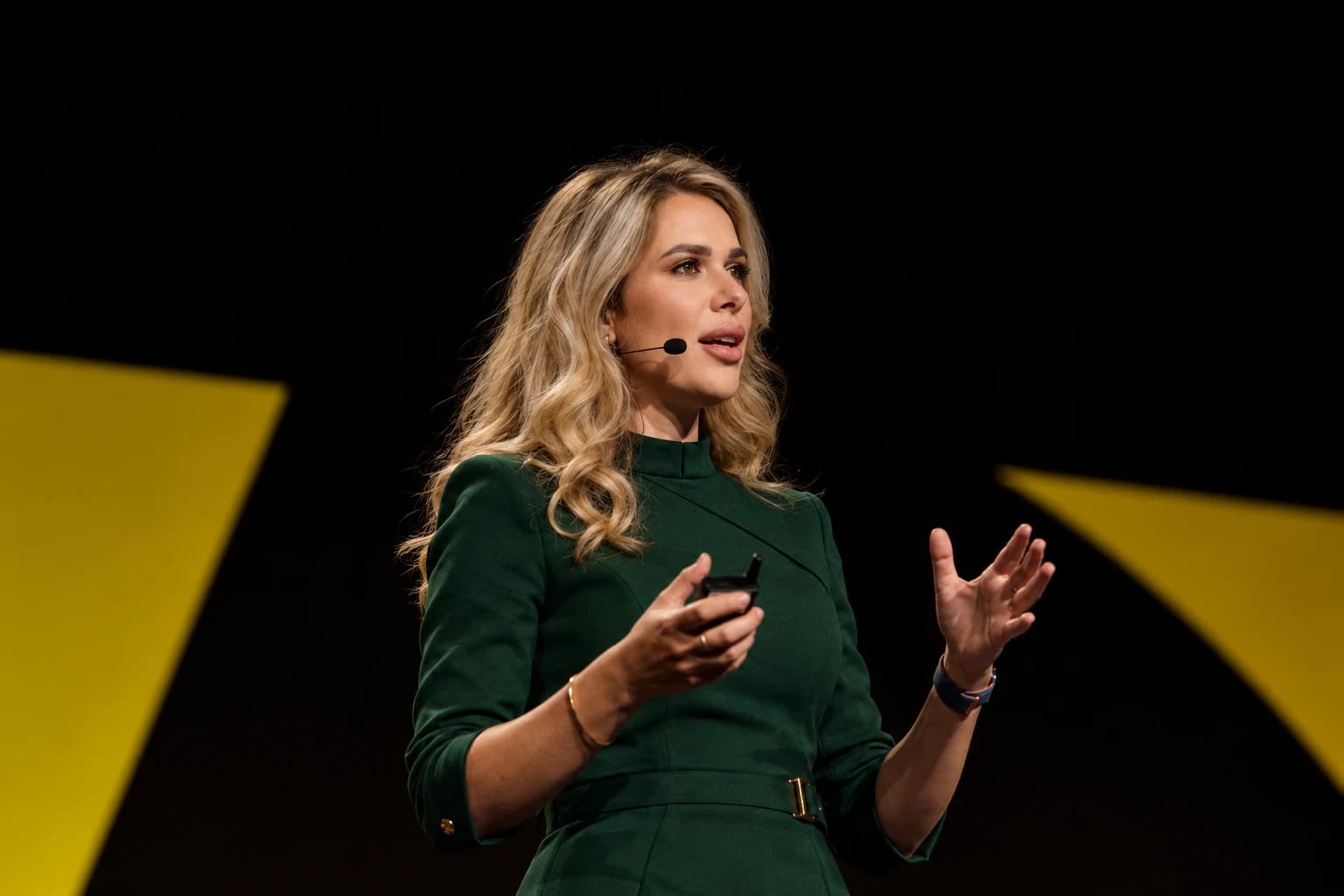 Iryna speaking on stage in a dark green dress with a headset microphone, gesturing as she talks