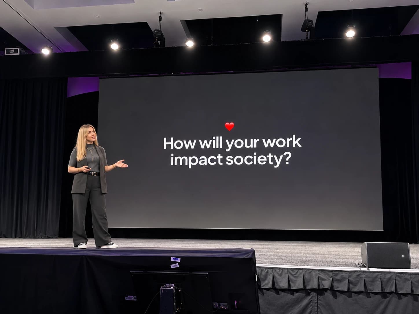 Iryna on stage beside a large screen that reads “How will your work impact society?”